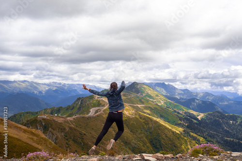 A young female tourist on top of a mountain jumps into the sky. Happiness and a sense of freedom 
