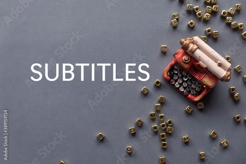 фотографія Top view of toys typewriter and gold alphabet beads on grey background written with Subtitles