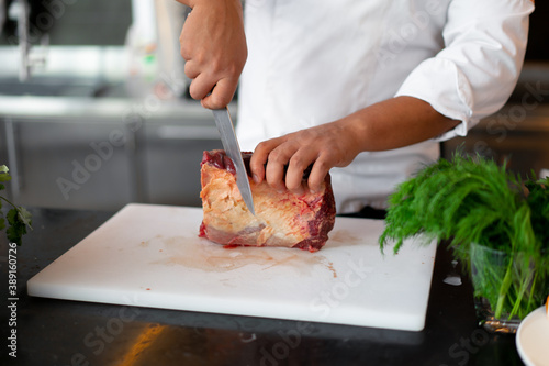 Fototapeta Naklejka Na Ścianę i Meble -  unrecognizable young African chef standing in professional kitchen in restaurant preparing a meal of meat and cheese vegetables.