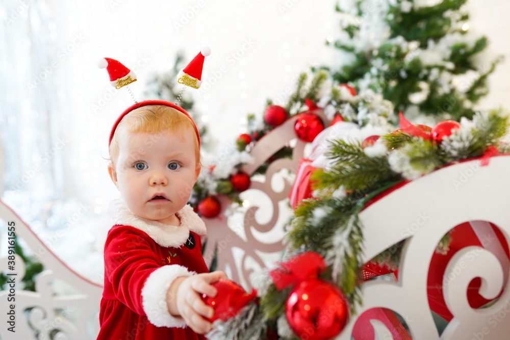 Little girl with red hair and blue eyes in Santa's red dress playing Christmas toys