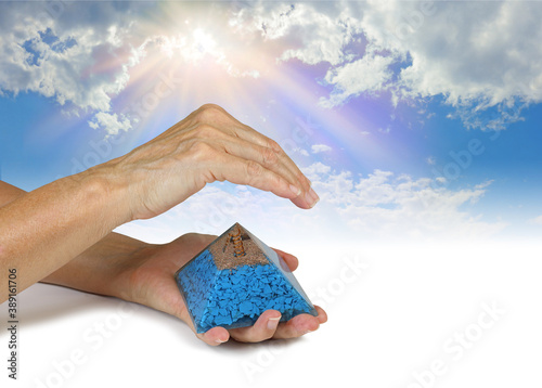 Sensing Orgone Pyramid Resonance on  Blue Sky background - Female holding an orgone pyramid in left hand with right hand hovering above sensing energy against blue sky background with copy space
 photo