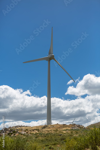 View of a wind turbine on top of mountains, cloudy sky as background © Miguel Almeida