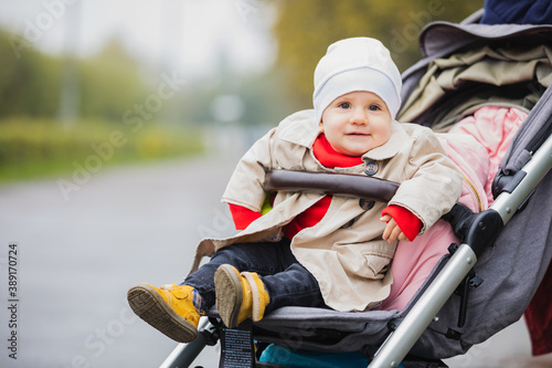 baby sitting in baby carriage, open eyes, in hat and jacket, winter or autumn time. Portrait.