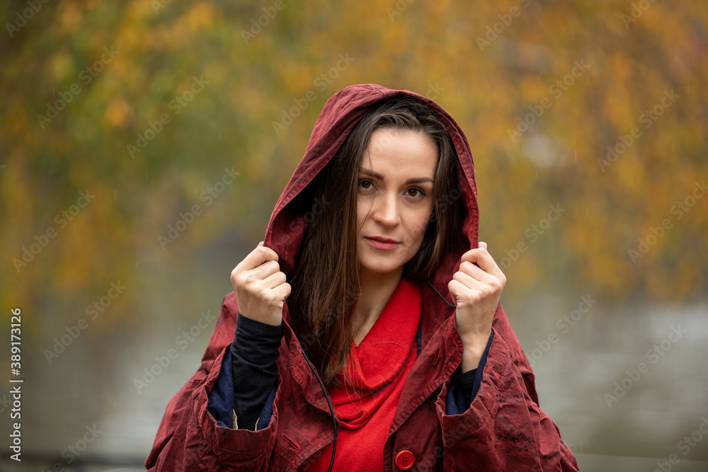 Portrait of a woman in hooded red raincoat walking in park on a rainy day