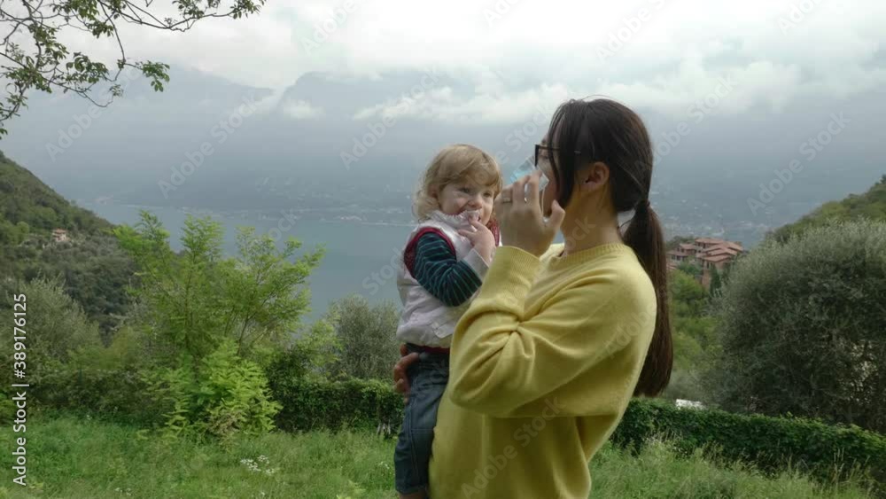 Young mother shows her curly, blonde, toddler son how she puts on her protection mask against covid-19 Young mother shows her curly, blonde, toddler son how she puts on her protection mask against covid-19