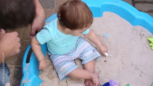 Little baby boy sits on sand in sandbox and plays with colorful toys on sandy background photo