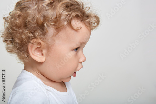 Adorable blonde baby looking at something with interest and opened mouth, side view of curious infant , copy space for advertisement for promotional text.