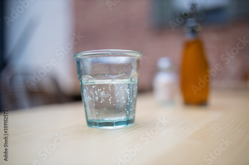 Glass of water on a wooden table with blurry bottles as background