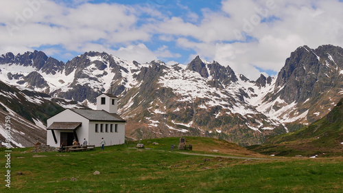 Hikers resting on benches in front of a small chapel near Silvretta reservoir, Montafon, Austria with beautiful mountain panorama in background with snow-capped mountains in early summer. © Timon