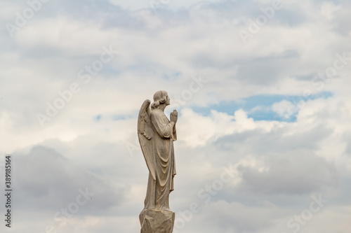 Escultura de anjo em topo de mausol  u dentro de um cemit  rio com c  u nublado ao fundo.
