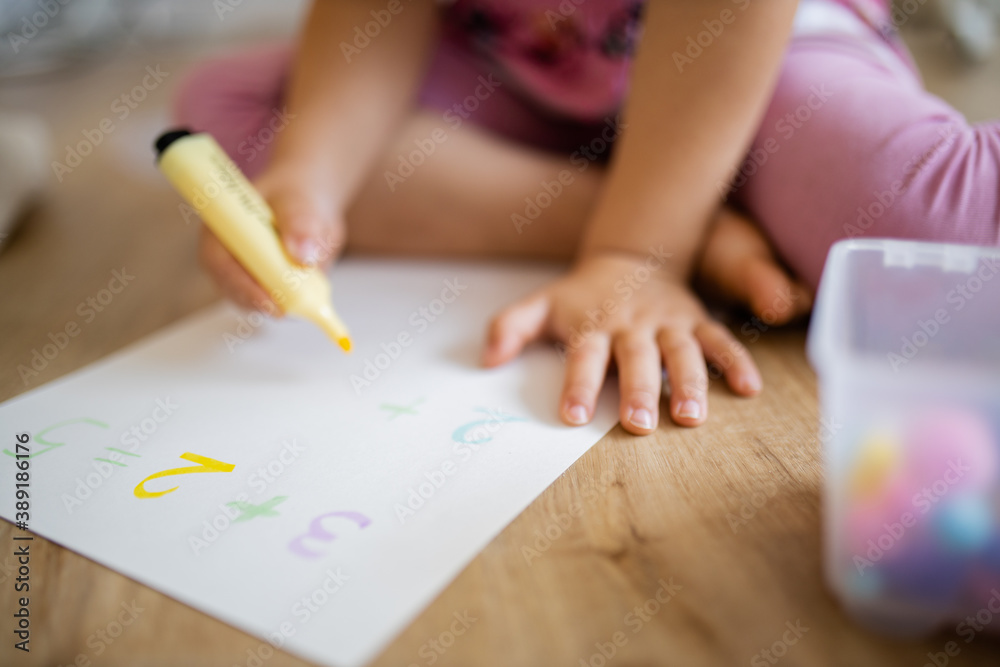 Little girl doing sums on a paper sheet with a textmarker on the wooden floor Little girl doing sums on a paper sheet with a textmarker on the wooden floor