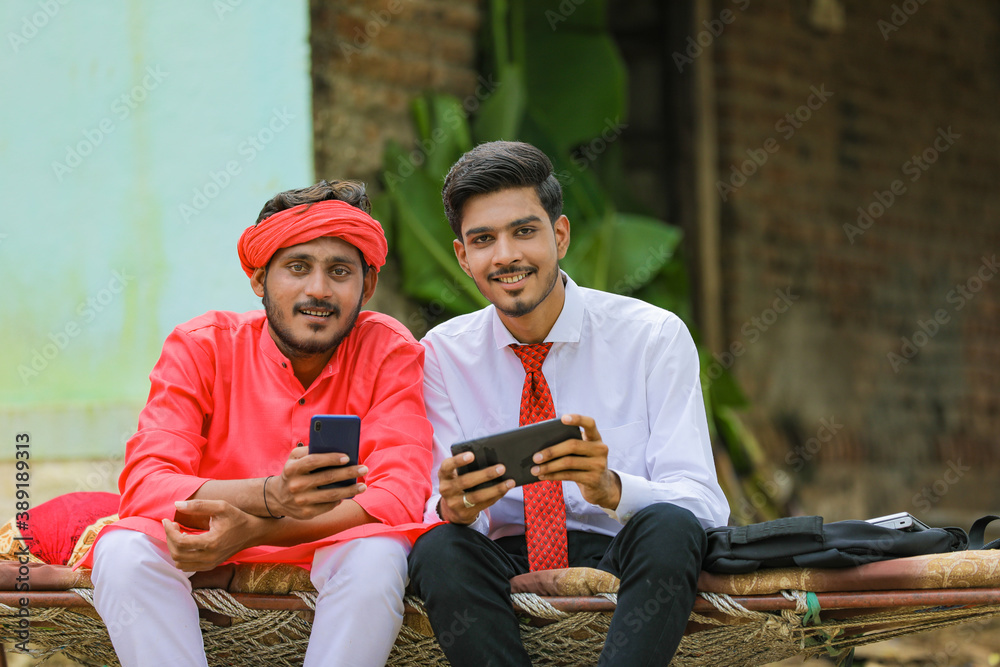 Fototapeta premium Young indian agronomist or banker showing some information to farmer in smartphone