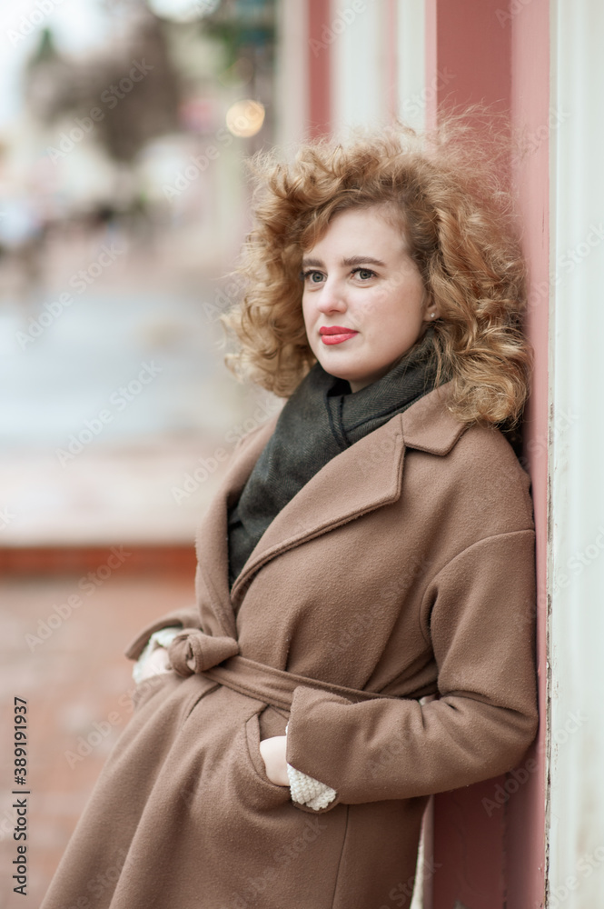 Portrait of a young woman with curly hair outdoors. Girl standing leaning against the wall