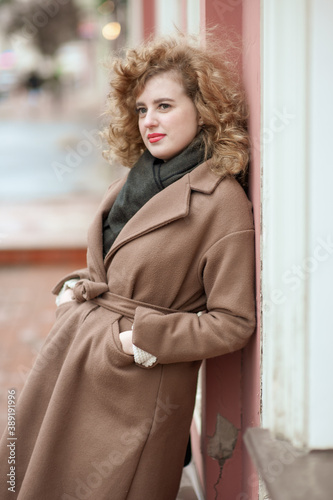 Portrait of a young woman with curly hair outdoors. Girl standing leaning against the wall