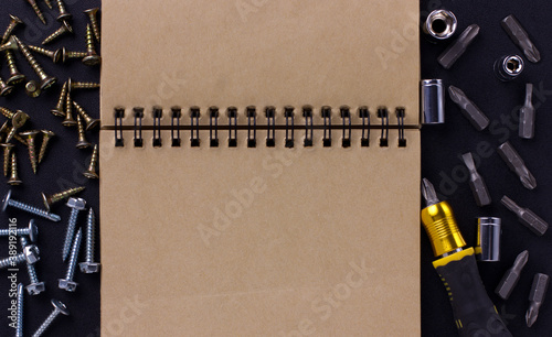 tools for repair and construction. Screwdriver with tips, furniture screws, measuring tape, self-tapping screws, notebook on a black background with a place for text. View from above