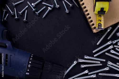 tools for repair and construction. Screwdriver, furniture screws, measuring tape, self-tapping screws, notebook on a black background with a place for text. View from above