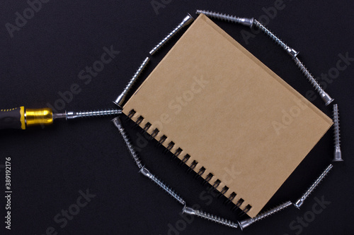 tools for repair and construction. Screwdriver, furniture screws, notebook on a black background with a place for text. View from above