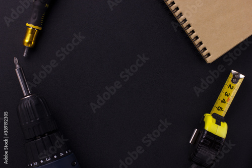 tools for repair and construction. Screwdriver, measuring tape, notepad on a black background with place for text. View from above