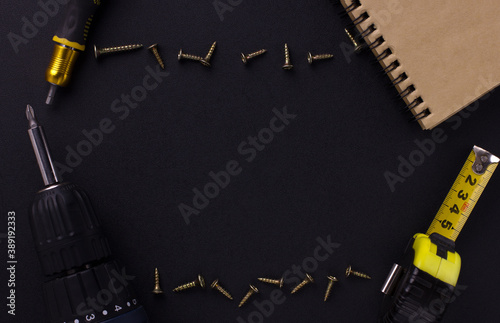 tools for repair and construction. Screwdriver, measuring tape, self-tapping screws, notebook on a black background with place for text. View from above