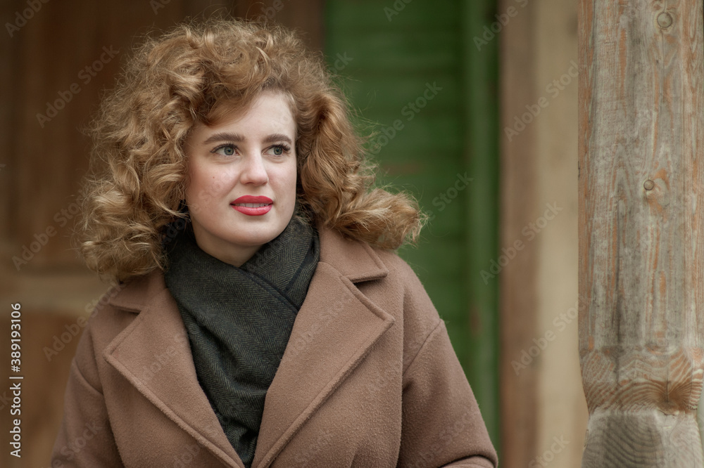 Portrait of a smiling young woman with curly hair on the porch of an old wooden house. Outside. Portrait of a smiling young woman with curly hair on the porch of an old wooden house. Outside.