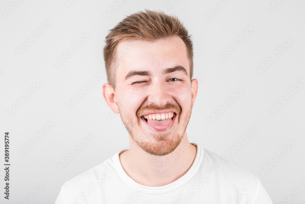 Positive funny male in white shirt, winks an eye and laughs at camera, demonstrates that everything is fine Positive funny male in white shirt, winks an eye and laughs at camera, demonstrates that everything is fine