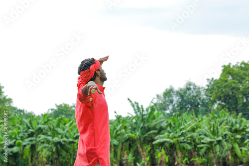 Young indian farmer in traditional wear and holding wooden stick in hand at field