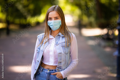 Portrait of happy young woman wearing protective face medical mask standing in park