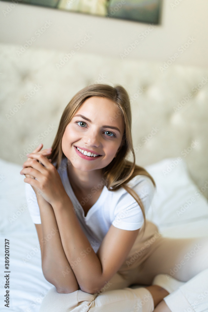 Smiling young woman sitting in bed at home Smiling young woman sitting in bed at home