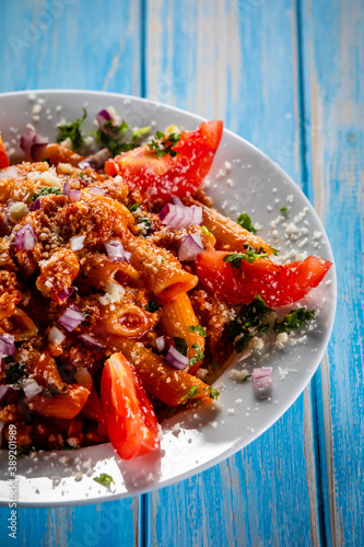 Penne with pork, tomato sauce, parmesan cheese, basil and vegetables served on wooden table
