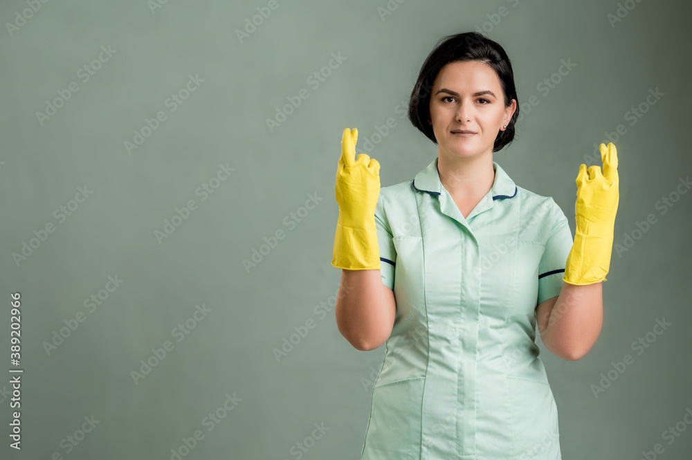 Young cleaning woman wearing a green shirt and yellow gloves showing good luck Young cleaning woman wearing a green shirt and yellow gloves showing good luck