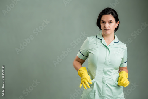 Young cleaning woman wearing a green shirt and yellow gloves showing empty pocket