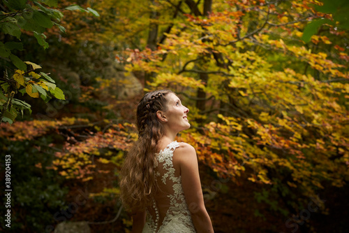 Back portrait of a beautiful bride looking up against an out of focus background of autumn trees.