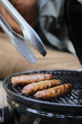 Мужчина готовит сосиски на компактном угольном гриле на улице.
A man cooks sausages on a compact charcoal grill outside.