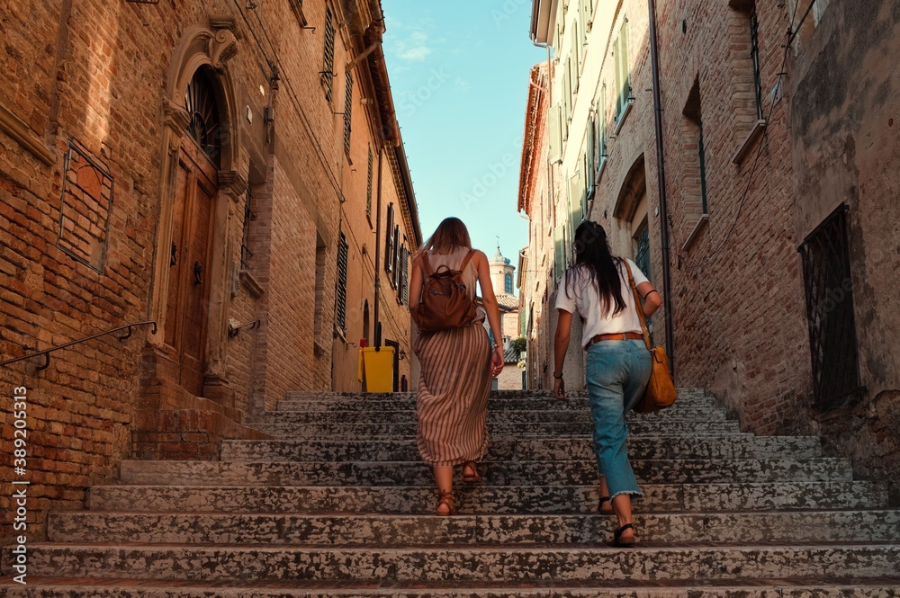 A couple of sisters is going upstairs in an alley of a medieval italian village (Corinaldo, Marche, Italy)