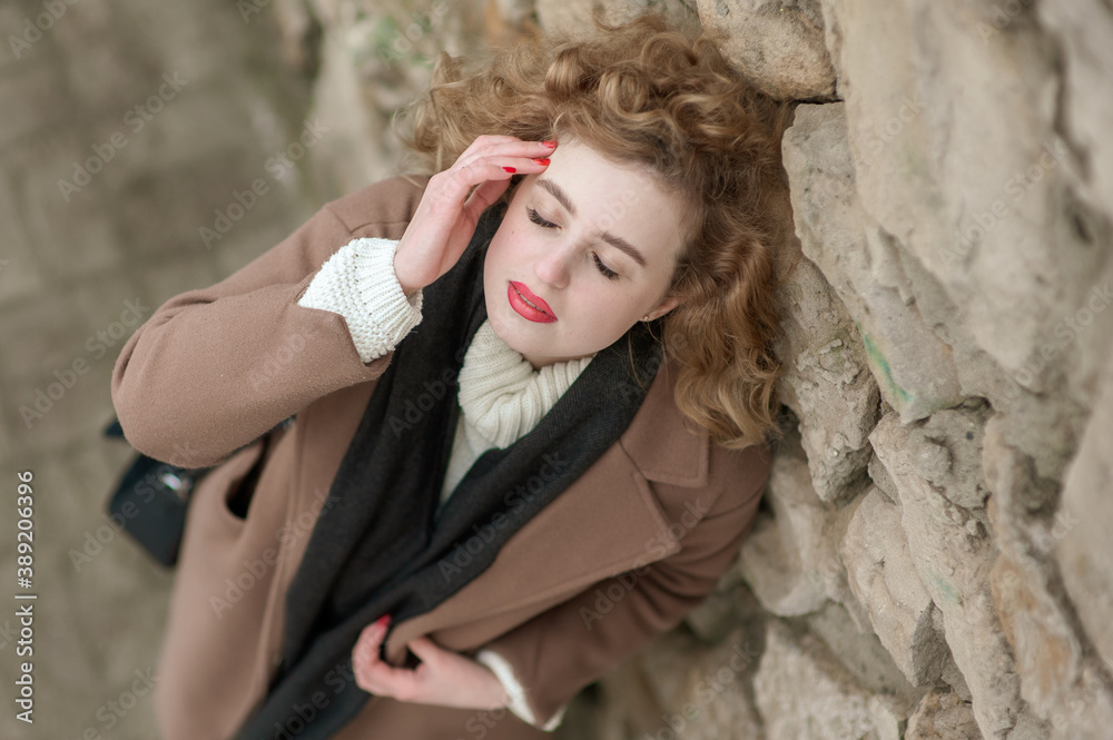 Portrait of a beautiful young woman near a stone wall. With closed eyes. Outside. View from above