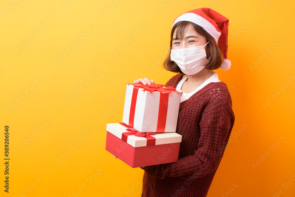 Portrait of young smiling woman in surgical mask wearing red Santa Claus hat isolated yellow background studio. Portrait of young smiling woman in surgical mask wearing red Santa Claus hat isolated yellow background studio.