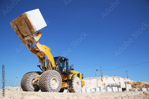 A big loader holding huge marble block. Loader machinery working on marble quarry with cloudy sky photo