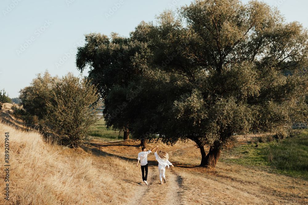 Back view of happy couple spends time together at nature. They walk through the road in the woods on a summer.
