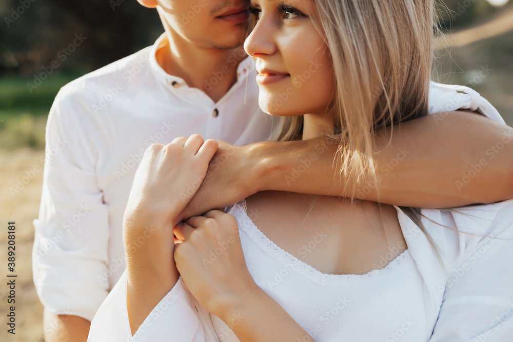 Close up cropped photo of happy blonde girl and passionate man. He hugs her from the back.