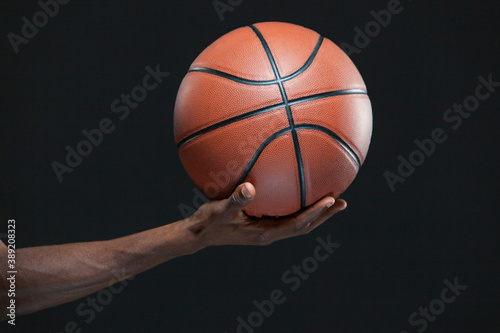 Photo of a black man hand holding a basketball isolated on black background. © satyrenko