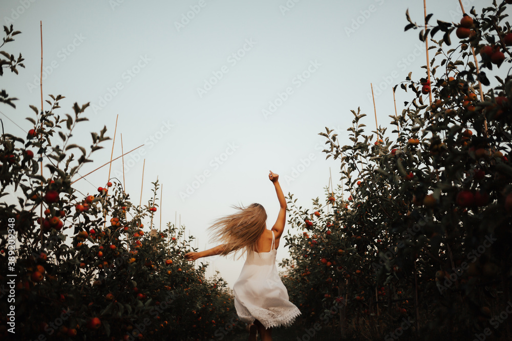 Back view of cheerful girl running and jumping in a apples garden. Selective focus and noise effect.