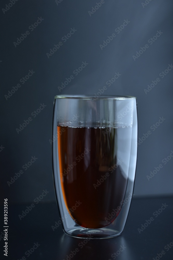 Double glass with black tea and steam on dark background Double glass with black tea and steam on dark background