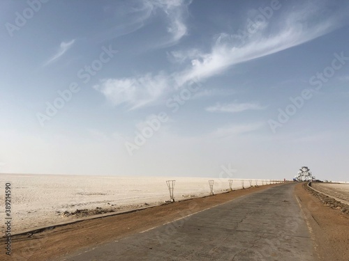 Beautiful empty path with  white sand on the sides and clear blue skies with few clouds.