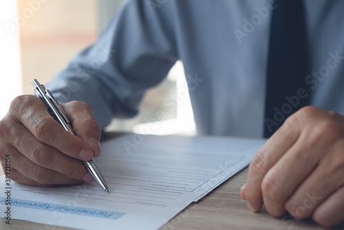 Close up of businessman with a pen in hand signing business contract on table in office