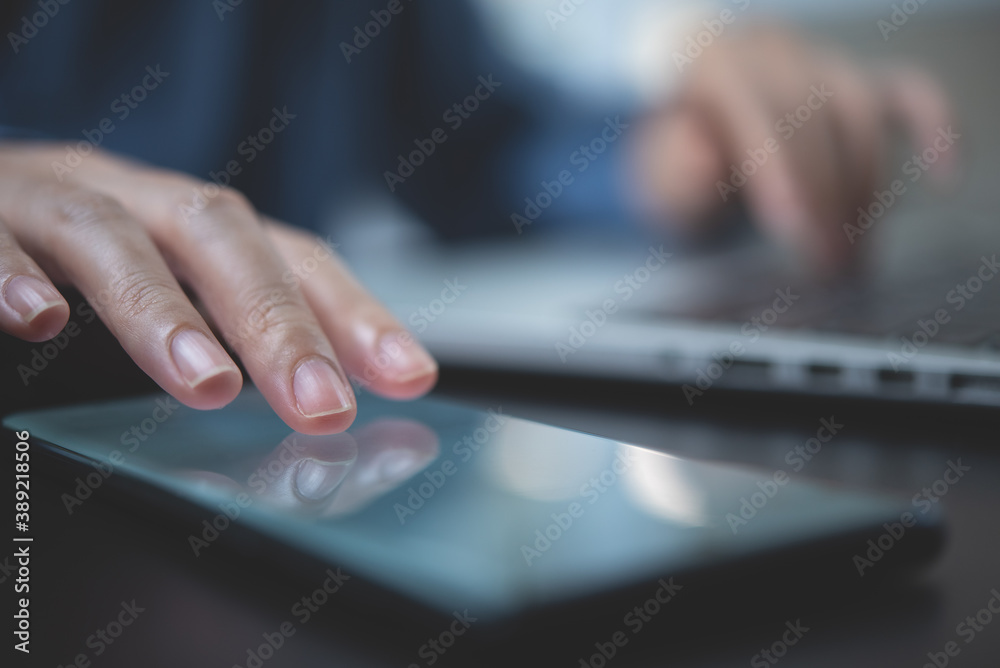 Close up of woman using and finger touching on mobile phone screen during working on laptop computer in office Close up of woman using and finger touching on mobile phone screen during working on laptop computer in office