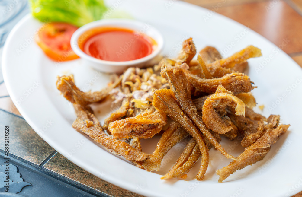 Deep-fried small fishes or Sillago fish with garlics. Crispy fried Sillago in white plate on table in resturant. Close up Thailand food image. Sillago or Pla Hed Cone in Thai language. Deep-fried small fishes or Sillago fish with garlics. Crispy fried Sillago in white plate on table in resturant. Close up Thailand food image. Sillago or Pla Hed Cone in Thai language.