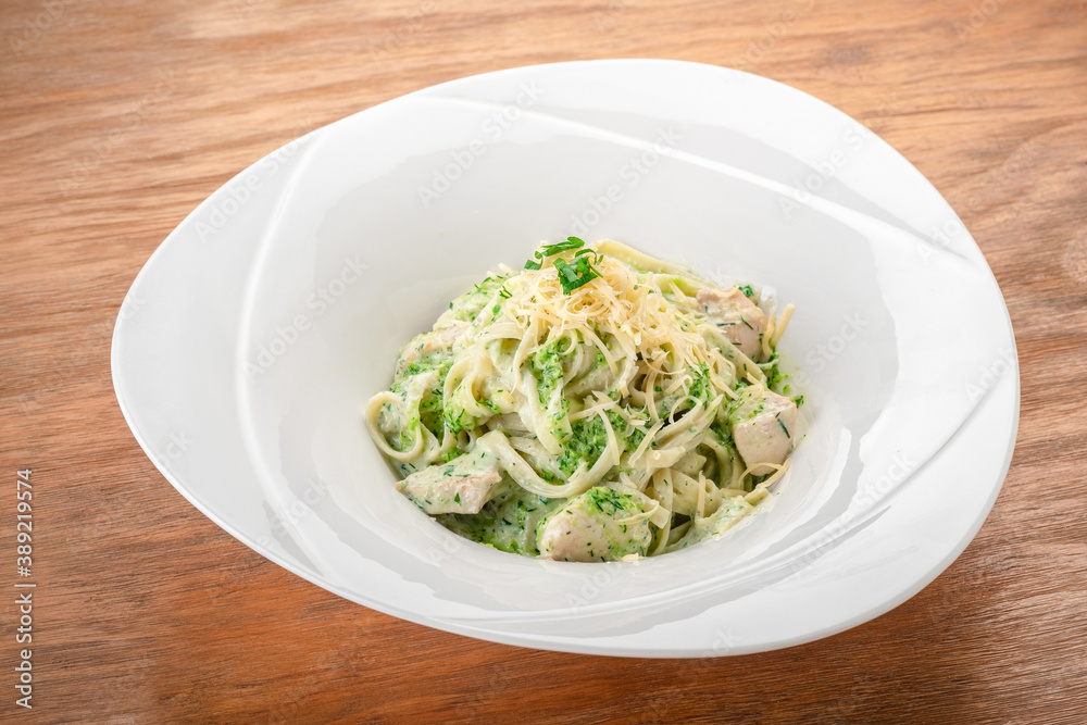 Tagliatelle pasta with pesto, chicken and Parmesan in a white plate on a wooden table