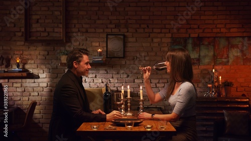 Elegant couple having romantic dinner at home  sitting at table in living room drinking red wine. Stay at home concept.