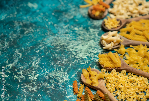 Various mix of dry pasta on wooden spoons.