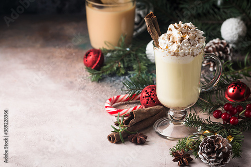 Traditional winter eggnog in glass mug with milk, rum and cinnamon, covered with whipped cream, christmas decorations